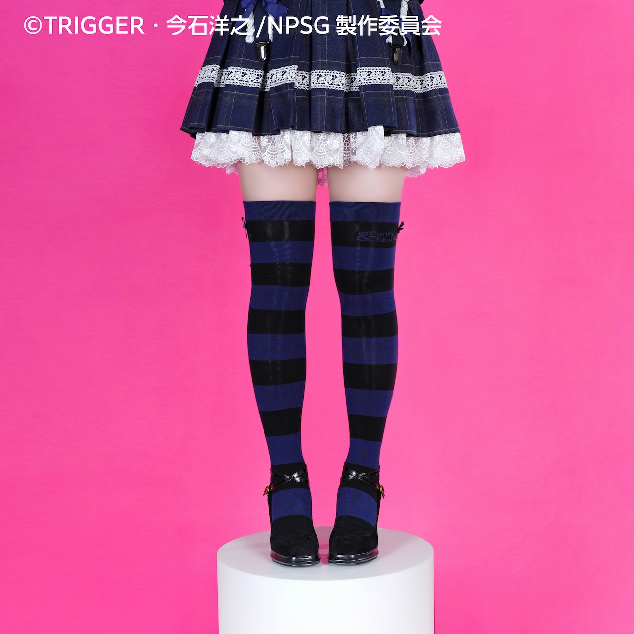 Front view of blue and black horizontal striped over-the-knee stockings worn with a skirt and black shoes against a pink background.