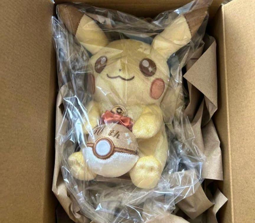 A Pokémon 30th anniversary Pikachu plush wrapped in clear plastic and packed inside a cardboard box.