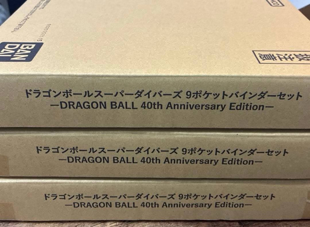 Three stacked unopened cardboard boxes labeled "DRAGON BALL 40th Anniversary Edition" for the Dragon Ball Super Divers 9-pocket binder set.