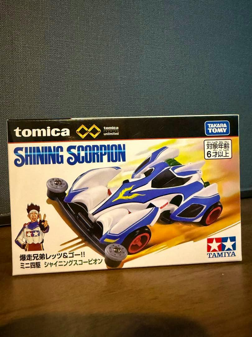 Box showing the Tomica Premium Unlimited "Shining Scorpion" mini 4WD toy packaging with an illustrated car and branding.