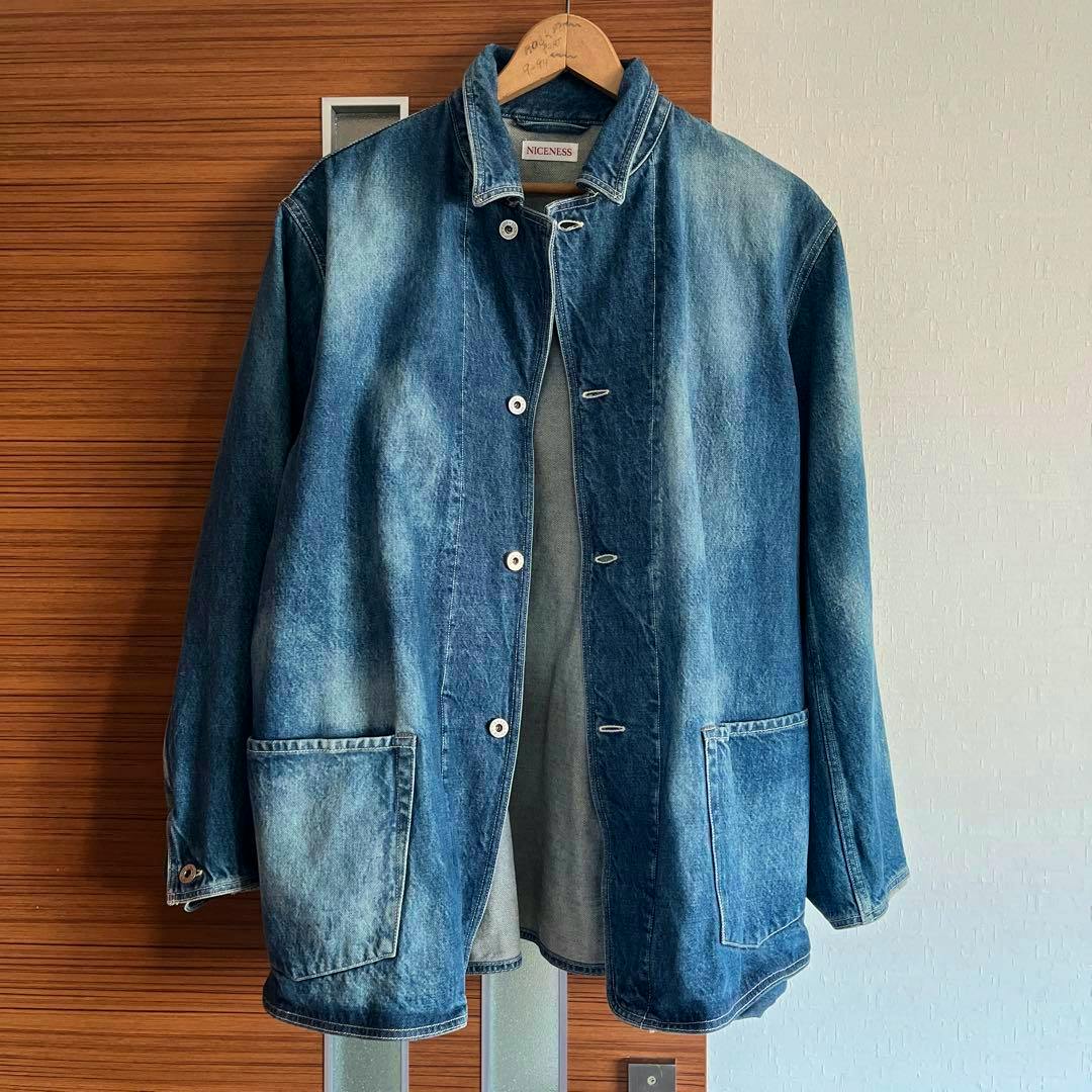 Blue cotton men's jacket hanging on a wooden hanger against a wood-paneled wall.