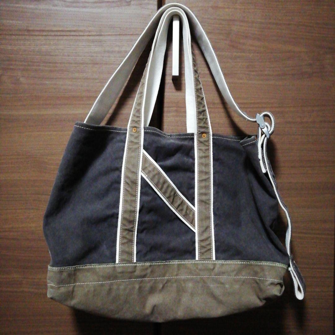 Front view of a NICENESS L.LESH shoulder tote bag hanging, showing the bag body with contrast trim, double handles, and a side adjustable strap.