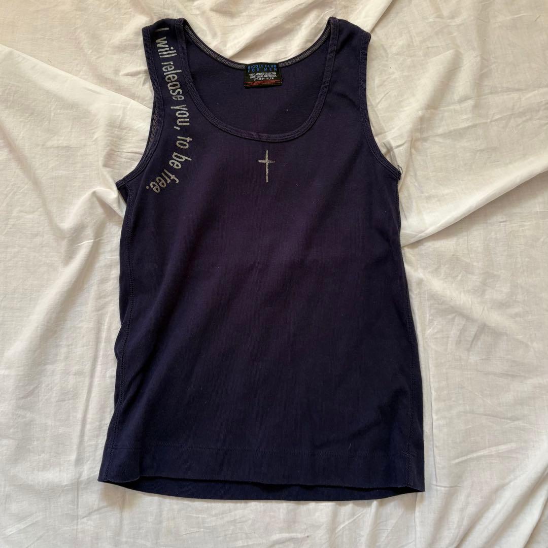 Women's purple tank top laid flat on a white background, showing a small cross detail at the chest and printed text along the left shoulder.