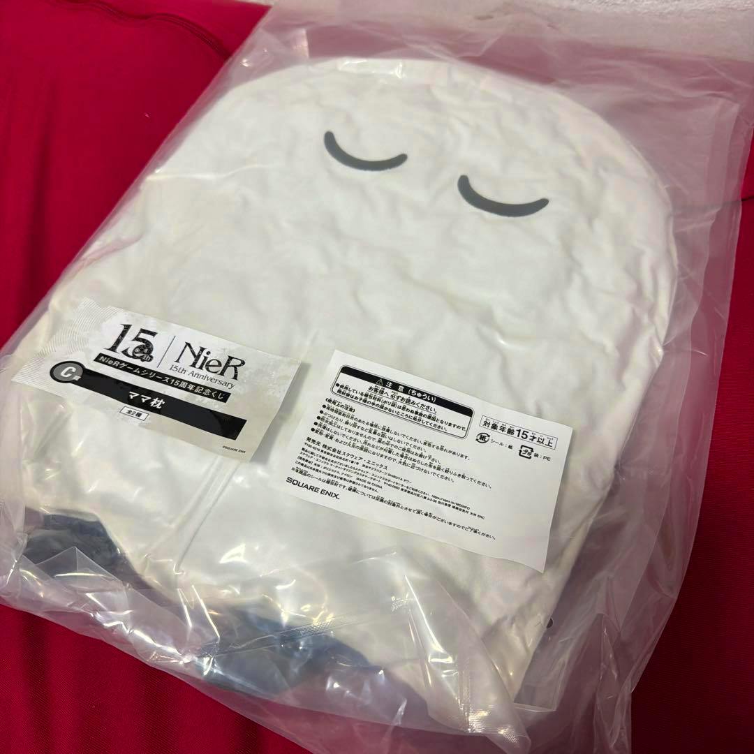 White NieR 15周年記念 ママ枕 plush pillow in plastic packaging showing closed eyes and product labels.