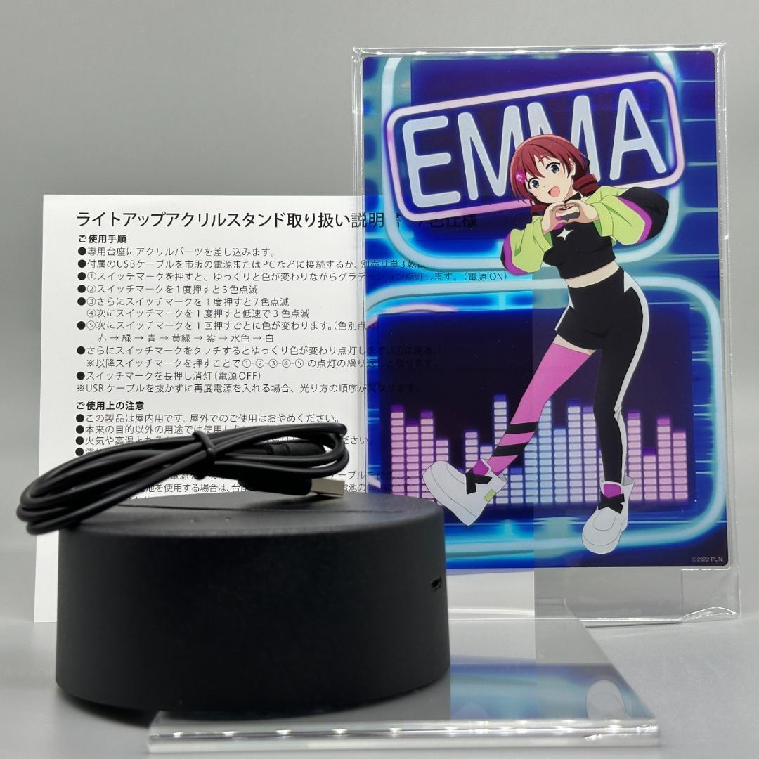 Photograph of the LED acrylic stand showing the Emma Verde character panel, black round base, USB cable, and instruction sheet.