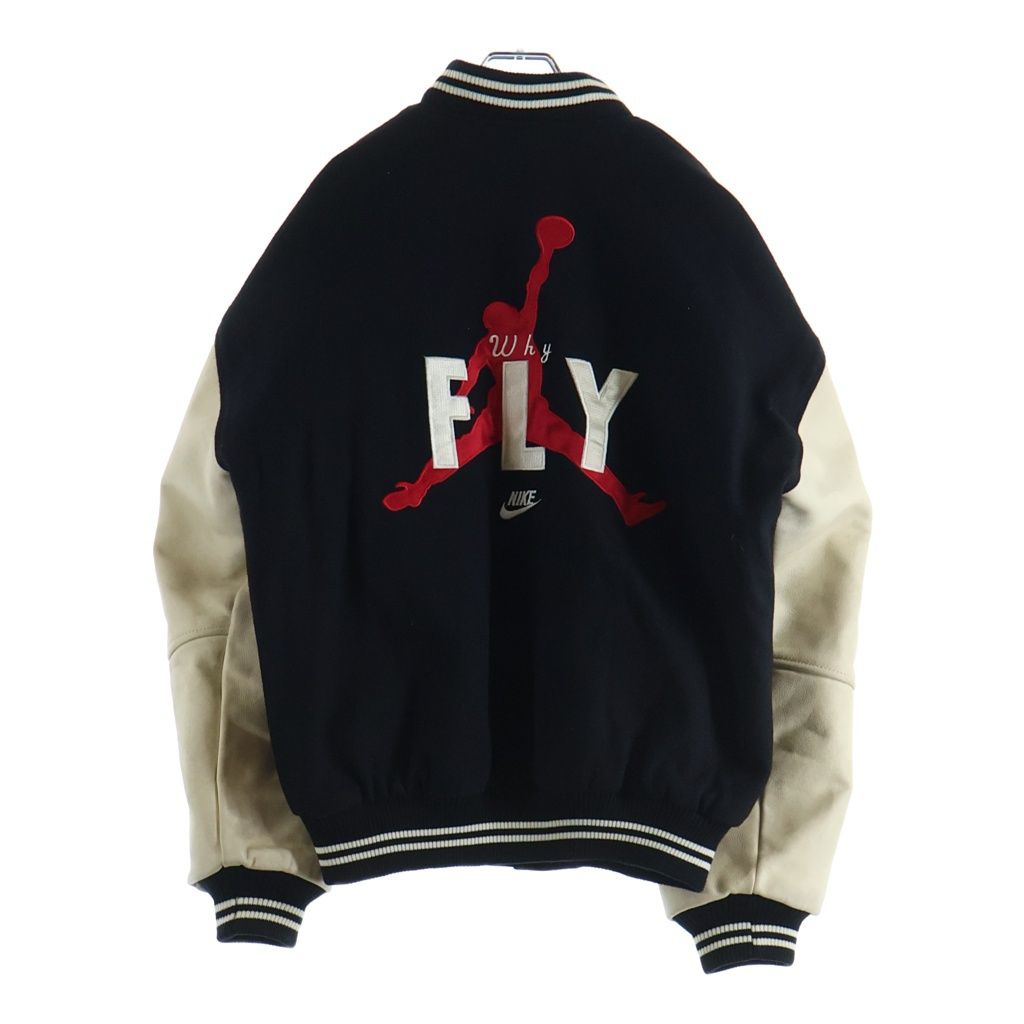 Back view of a black and beige NIKE 90s Air Jordan varsity jacket with contrasting leather sleeves and a large "FLY" graphic.