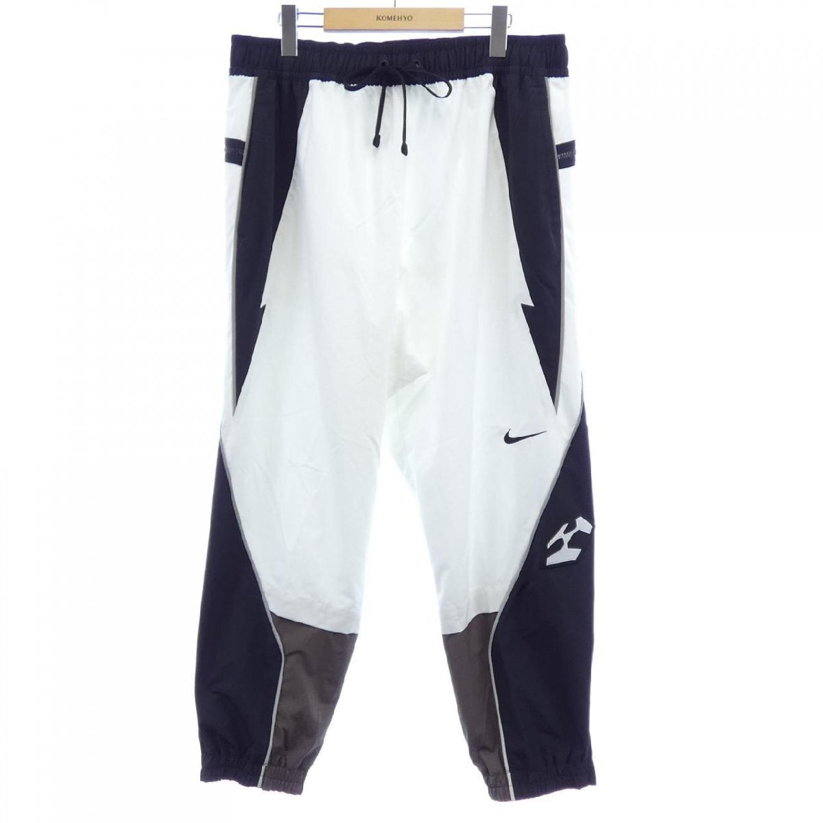 Front view of Nike ACRONYM men's polyester pants in white and black hanging on a hanger.