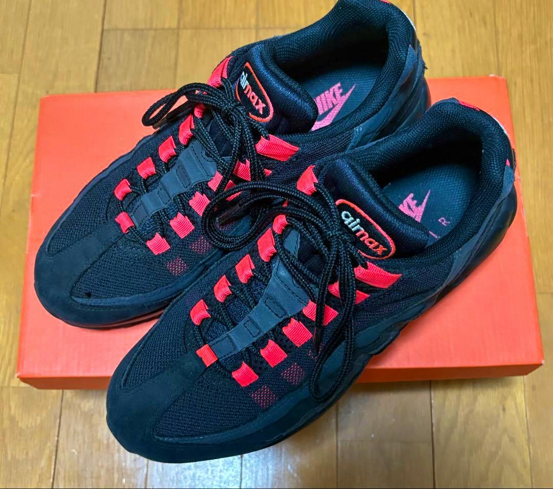 Pair of black and laser crimson Nike Air Max 95 sneakers shown on an orange shoebox from above.