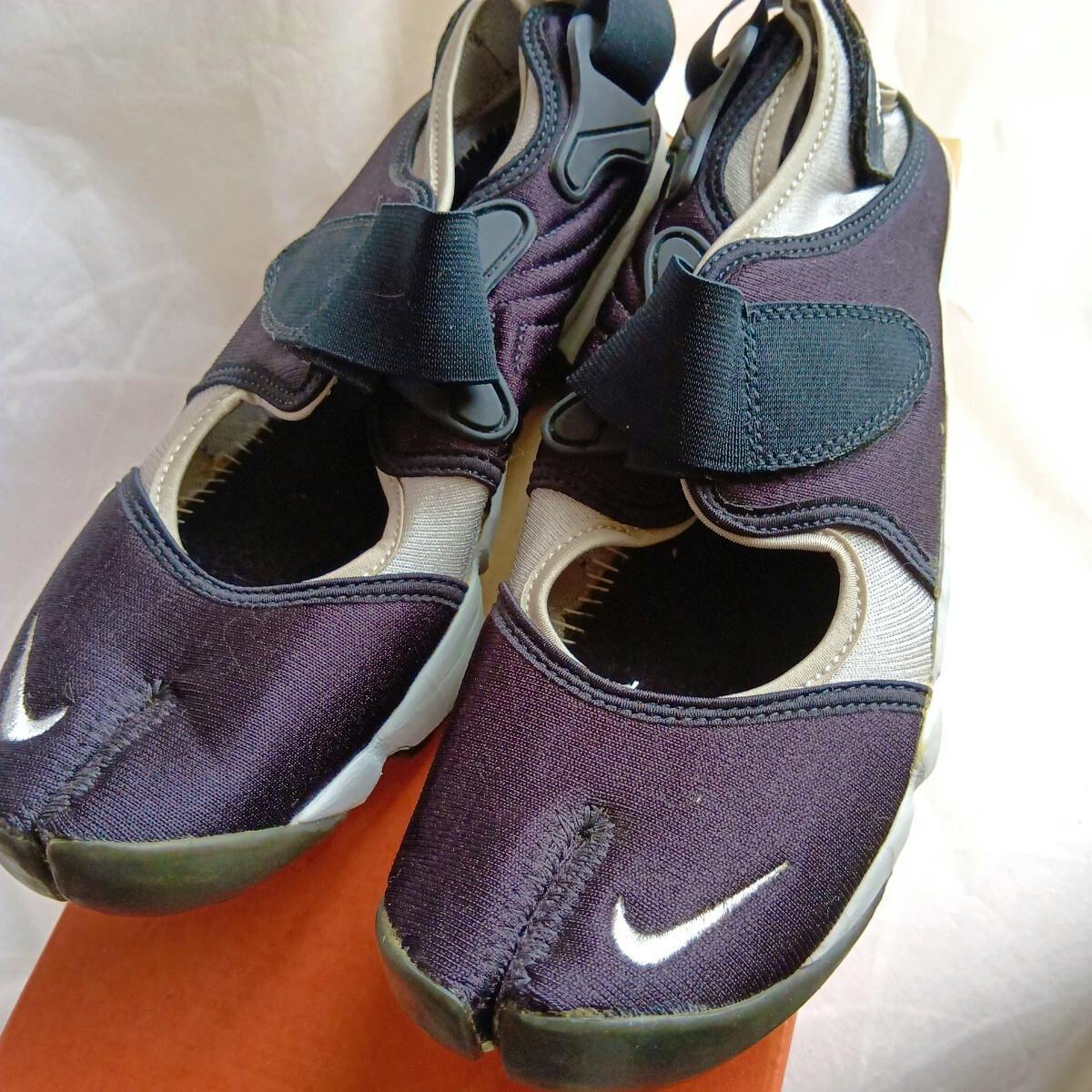 Close-up photo of NIKE AIR RIFT B shoes in black/metallic silver showing the split-toe design and velcro straps.