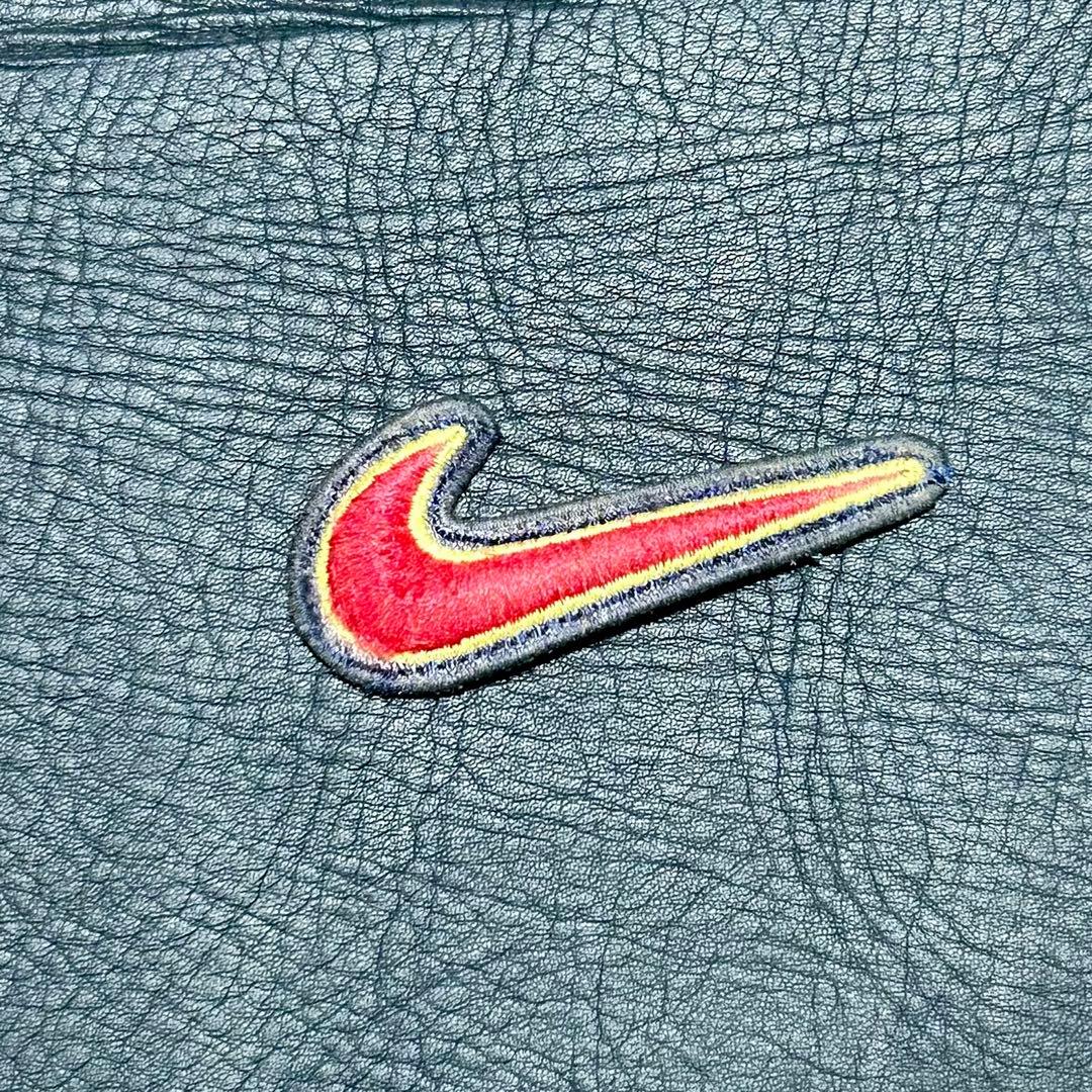 An embroidered Nike Swoosh patch with red fill and yellow outline on a dark textured background.