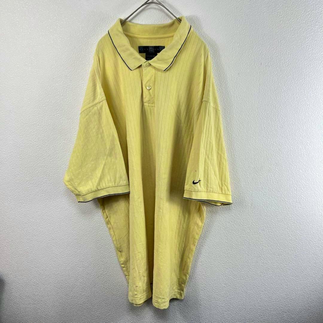 Yellow oversized Nike golf polo shirt hanging on a hanger against a white wall, front view with collar, button placket, and Nike swoosh on the left sleeve.