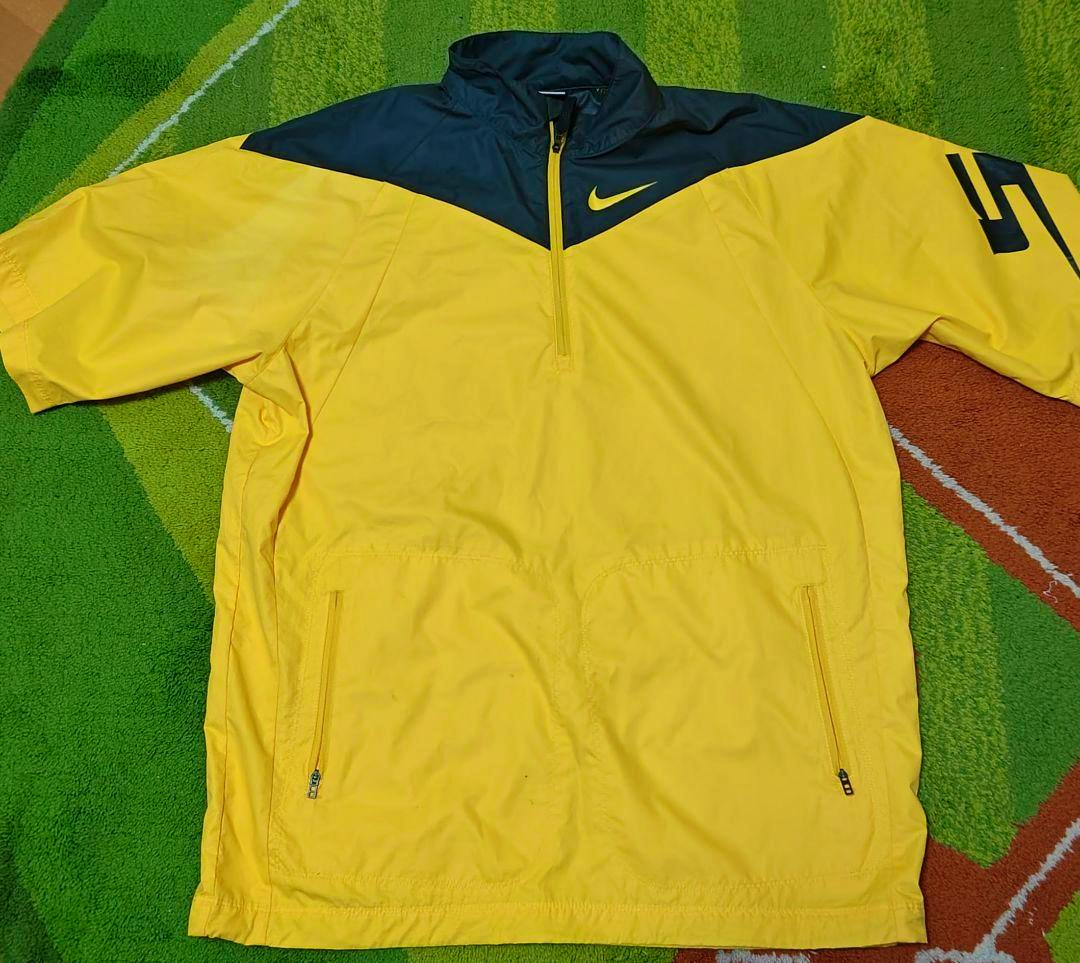 Yellow and black Nike men's polyester golf jacket laid flat showing the front with a quarter-zip, zippered pockets, and a graphic on the sleeve.