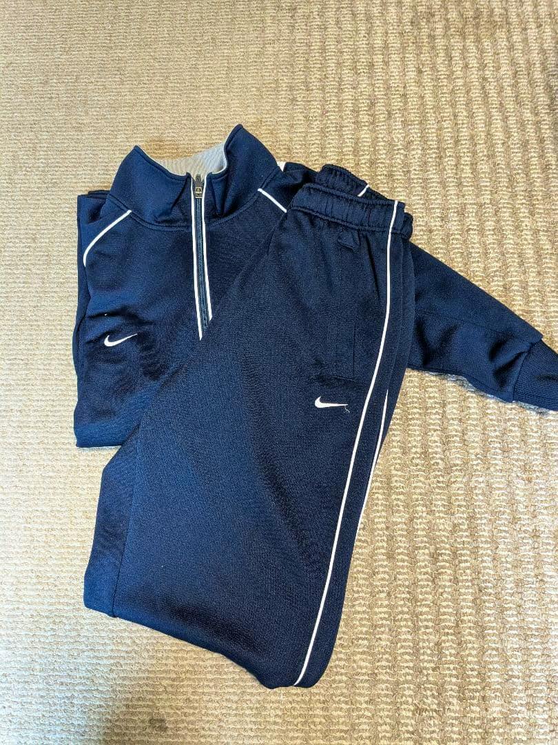 Folded navy Nike track jacket and matching pants laid flat on a carpet.
