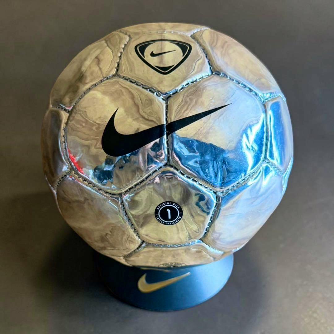 Metallic silver Nike Scorpion commemorative soccer ball with black swoosh displayed on a dark stand.