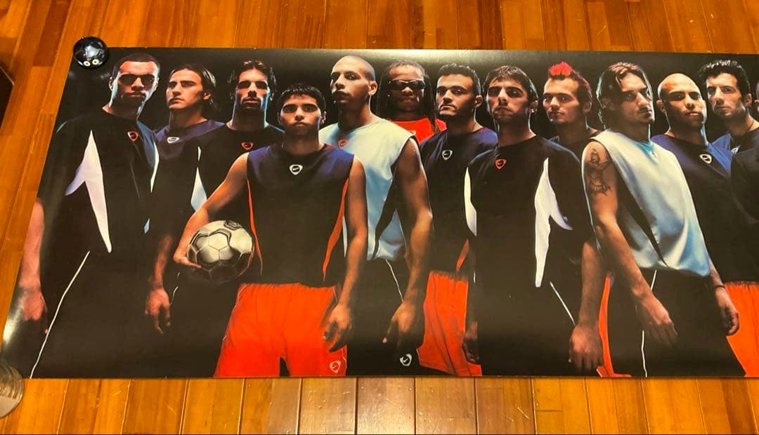Photograph of the poster showing a lineup of soccer players wearing black, light-blue, and orange Nike kits and holding soccer balls.