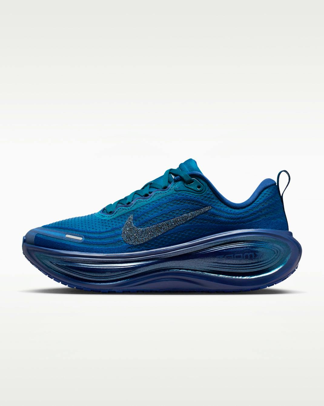 Side profile of a blue Nike Vomero Plus sneaker featuring Swarovski® crystals on the Swoosh.