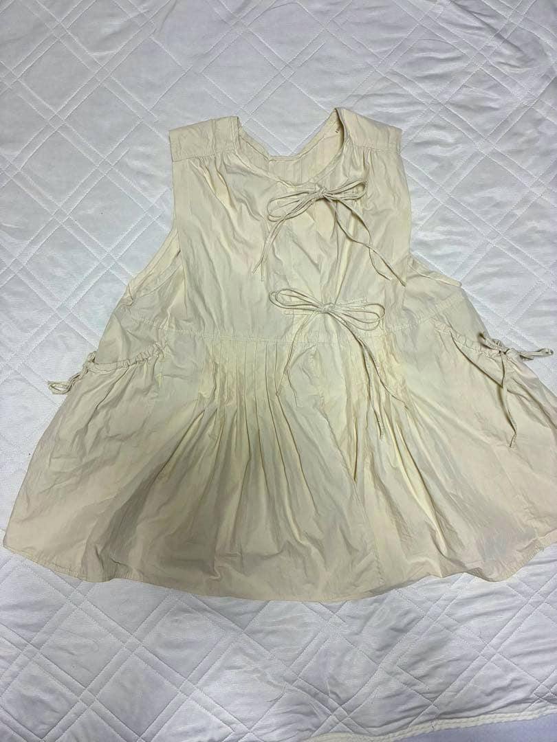 Ivory ribbon-detail vest laid flat showing the front with two tied bows and pleated lower section.