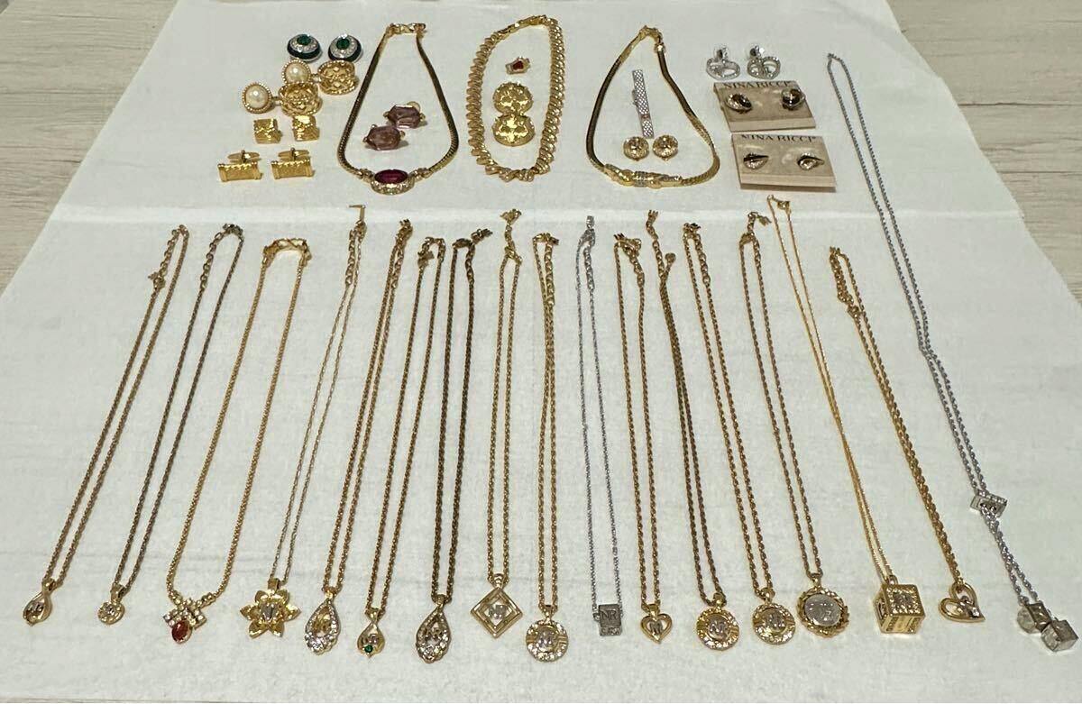 Multiple Nina Ricci necklaces and other accessories laid out on a white cloth, showing chains and pendants.