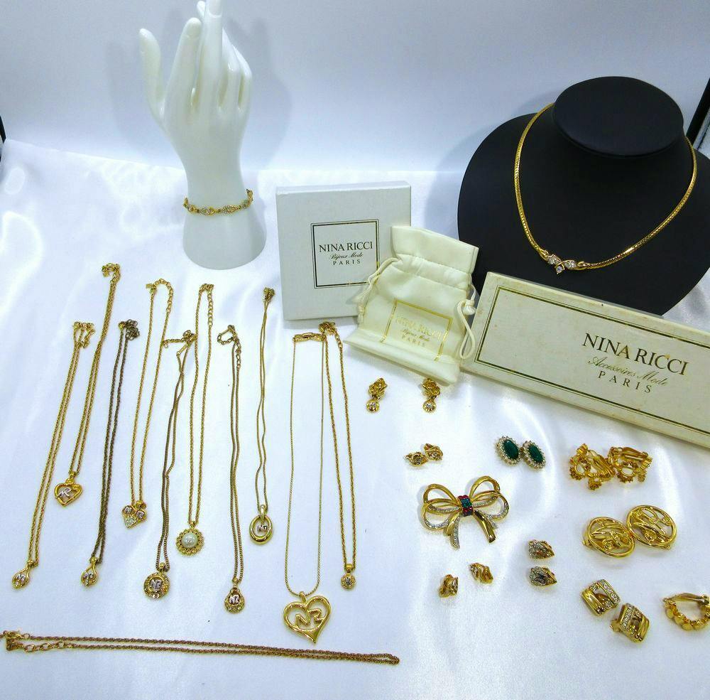 Several Nina Ricci gold-tone necklaces and other jewelry displayed on a white surface with one gold necklace on a black bust.