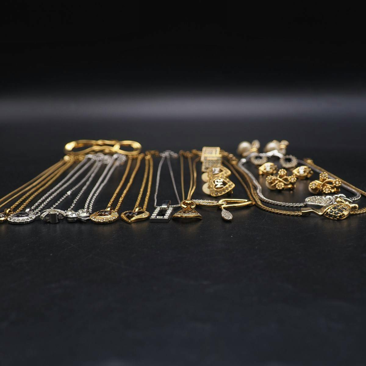 Multiple gold- and silver-toned necklaces and assorted Nina Ricci accessories arranged on a black surface.