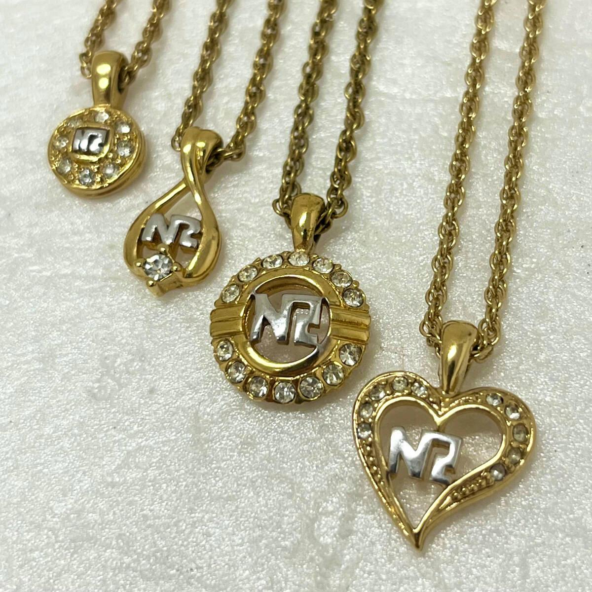 Four gold Nina Ricci pendant necklaces with rhinestones arranged on a white background.