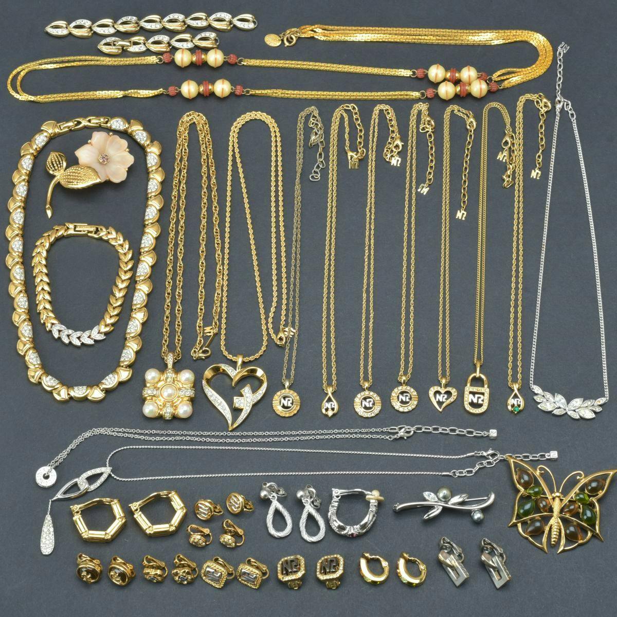 Flat lay of thirty gold-tone Nina Ricci necklaces, pendants, brooches and earrings with rhinestones on a dark background.
