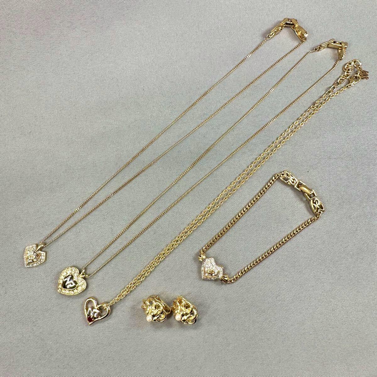 Five-piece NINA RICCI gold-color jewelry set arranged on a gray background showing three necklaces, one pair of earrings, and one bracelet.
