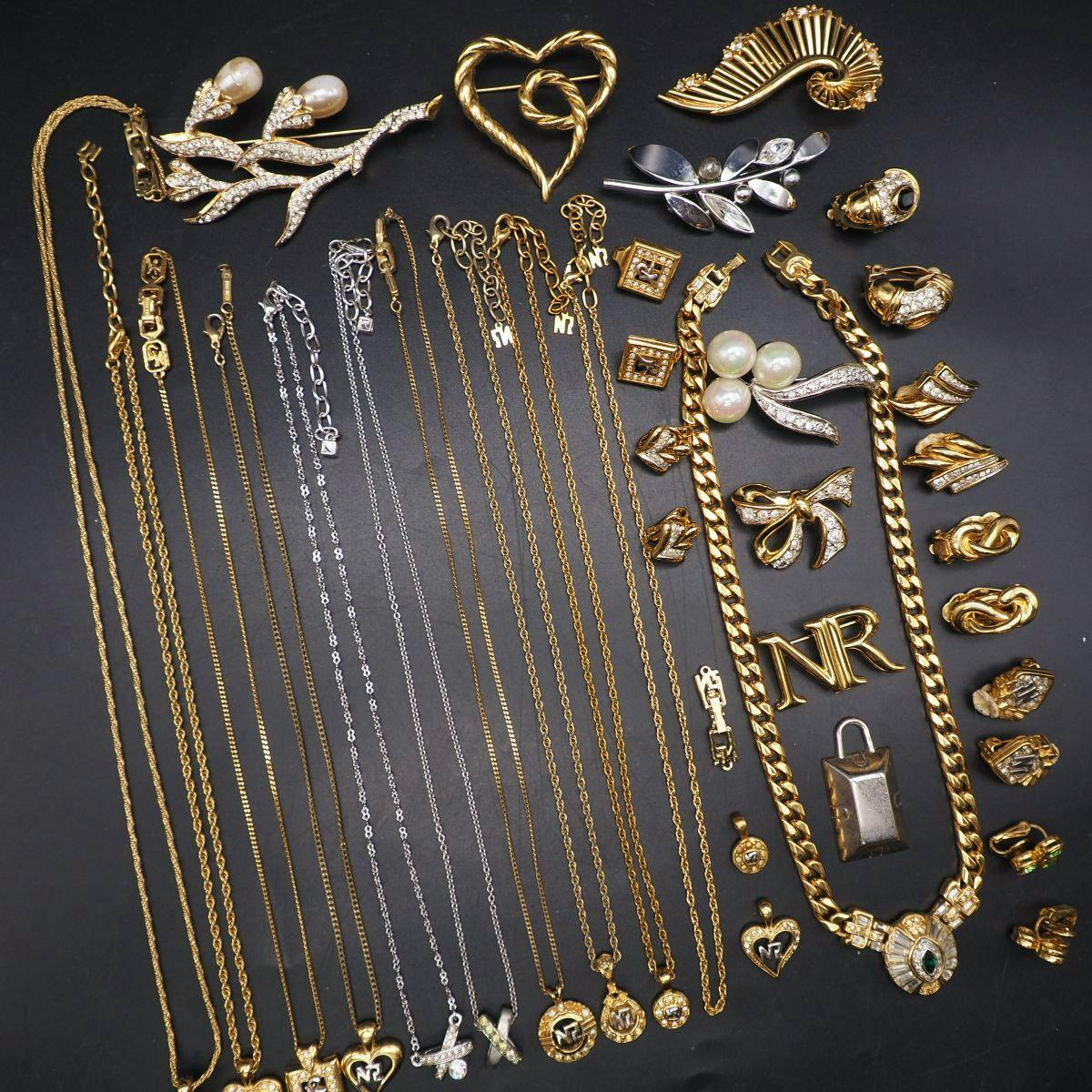 Flat lay of many Nina Ricci gold- and silver-tone necklaces, pendants, brooches, and earrings arranged on a dark background.