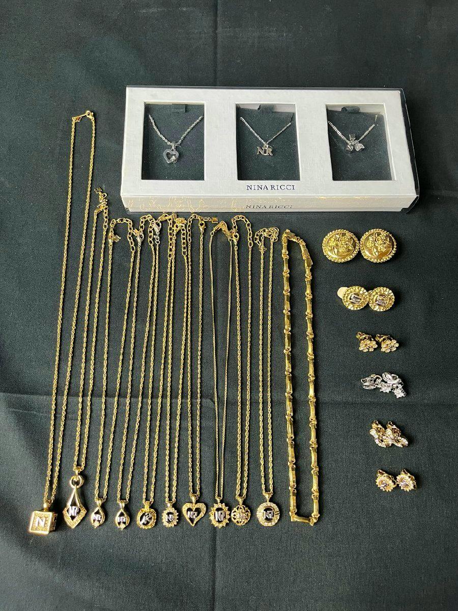 Assortment of Nina Ricci necklaces and earrings laid out on black fabric, including a boxed set of silver pendants and multiple gold-tone chains with logo and heart charms.
