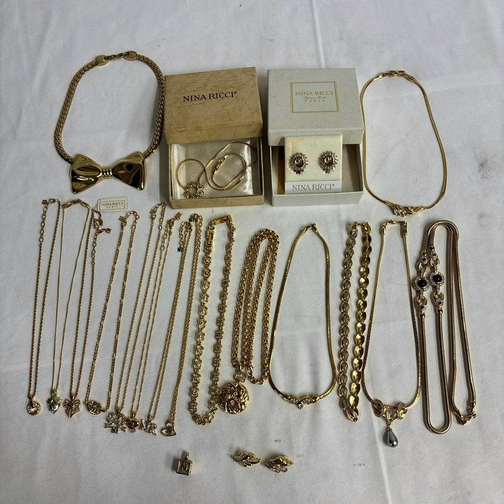 A collection of about 20 Nina Ricci accessories including necklaces, bracelets, earrings, and pendant tops arranged on a white background with two Nina Ricci boxes.