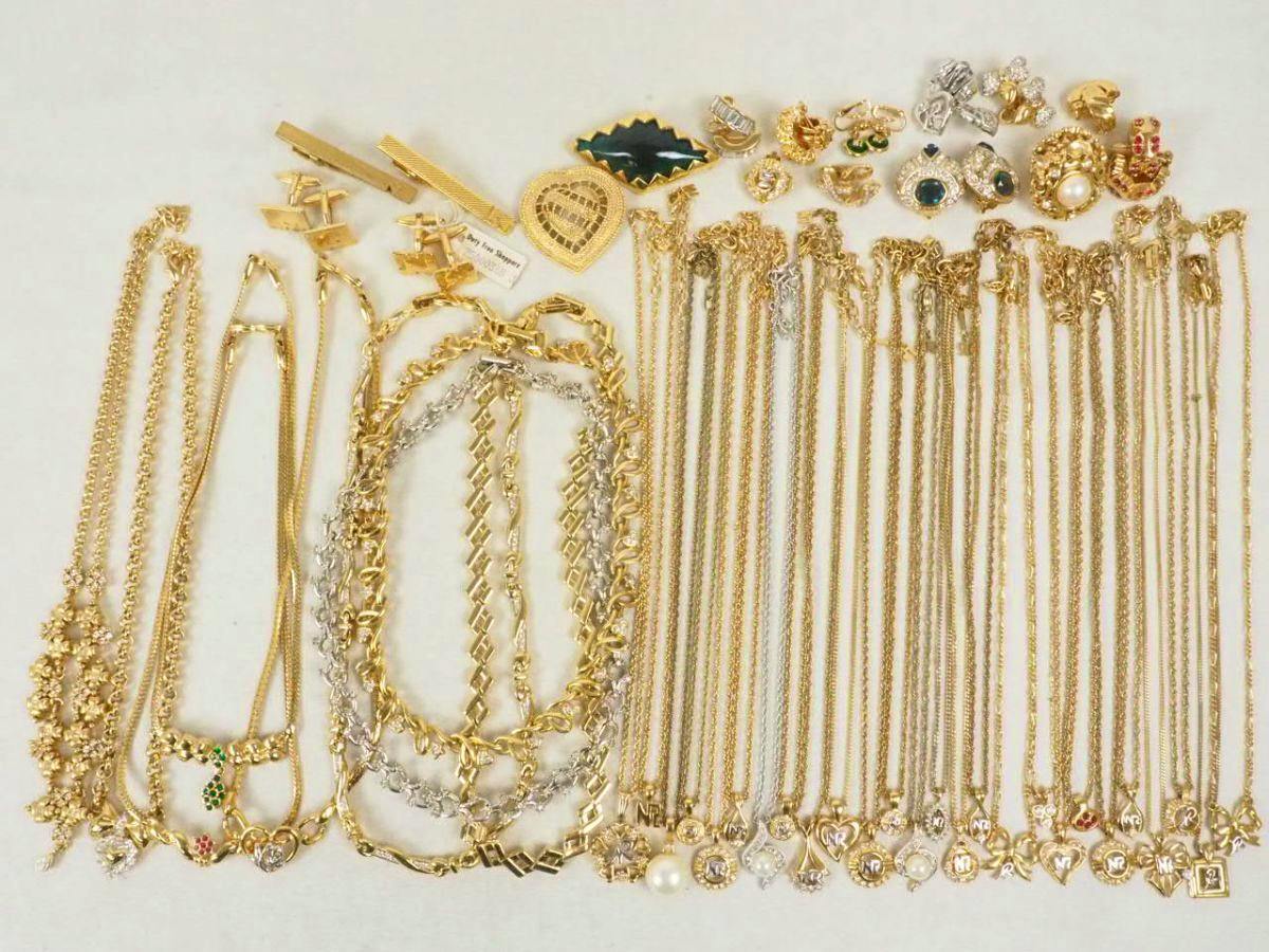 A laid-out collection of gold-tone necklaces, chains, pendants and brooches on a light background.