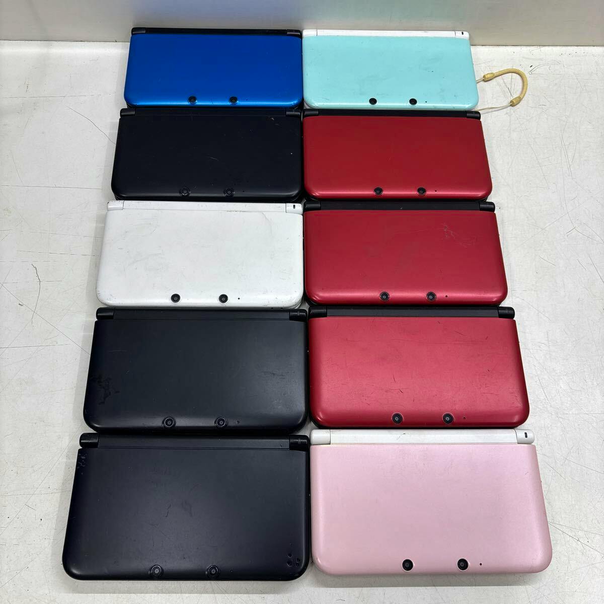 Ten Nintendo 3DS LL handheld consoles in various colors shown closed and arranged in a grid on a white surface.