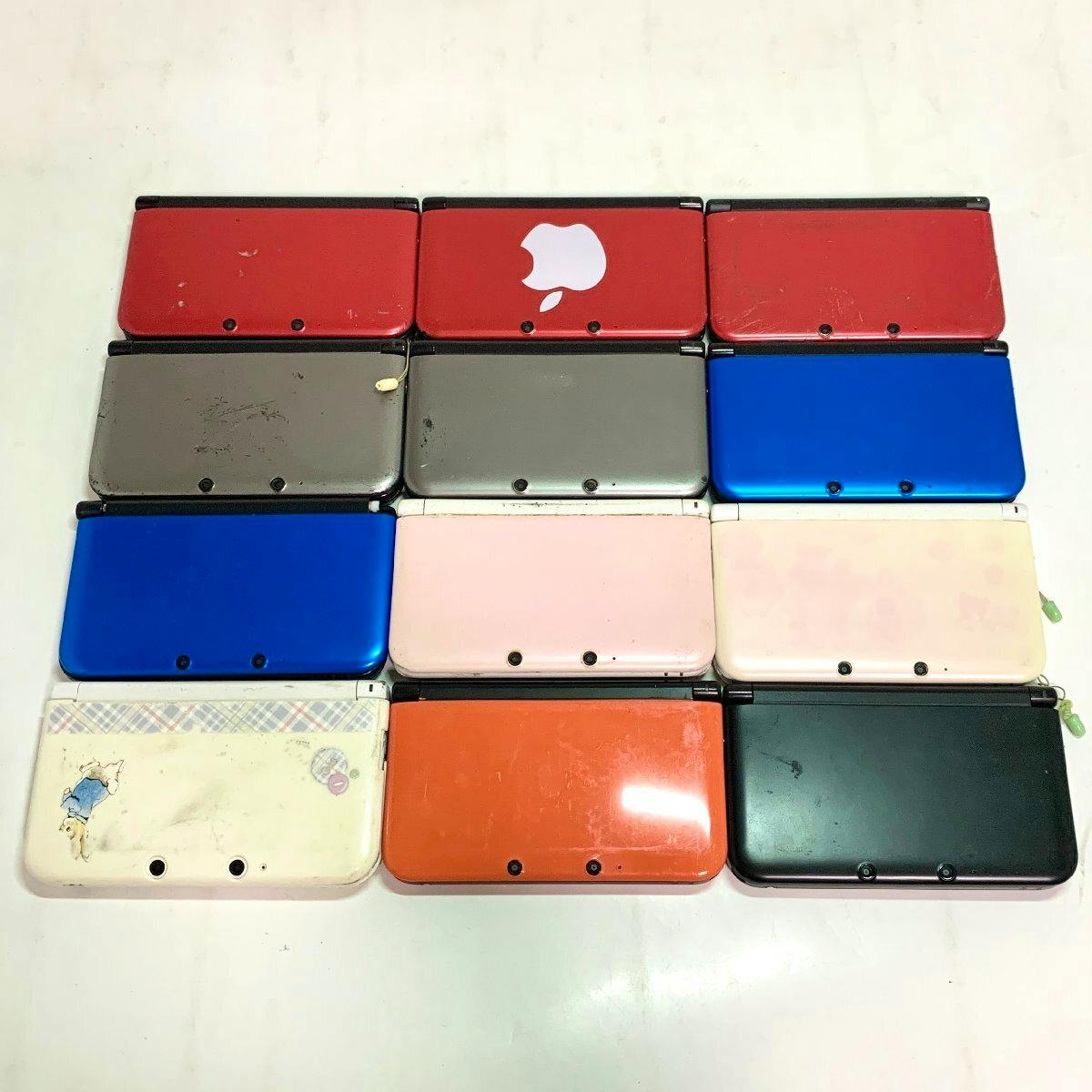 Twelve Nintendo 3DS LL handheld console units shown closed and arranged in rows, with various colors and visible wear.