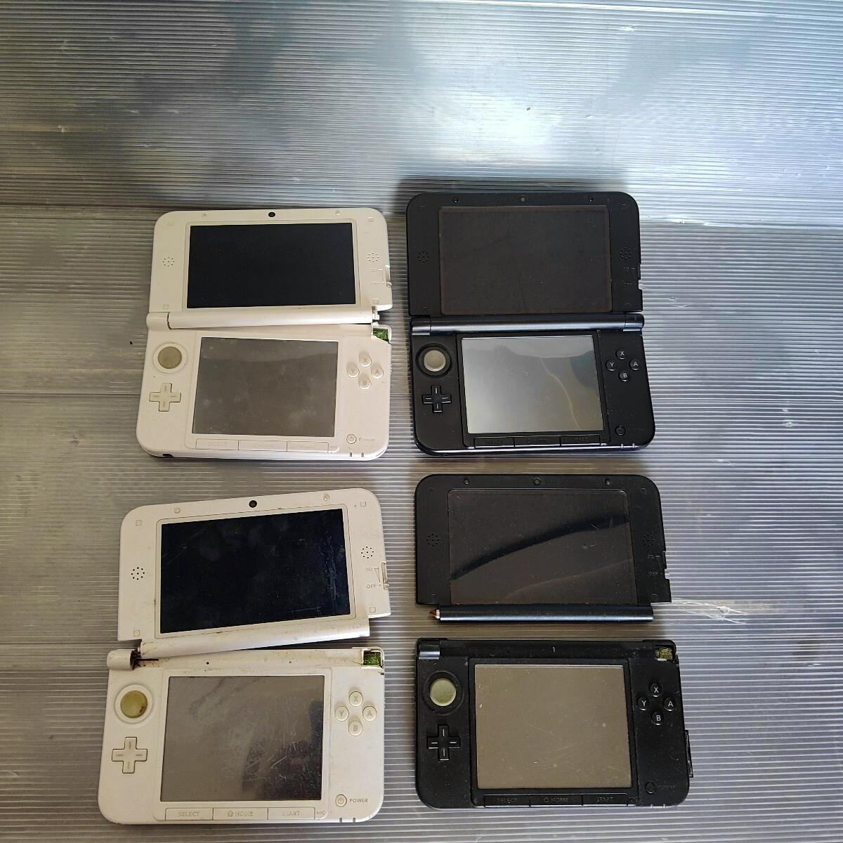 Four Nintendo 3DS LL handheld consoles (two white, two black) shown opened on a corrugated surface with visible wear.