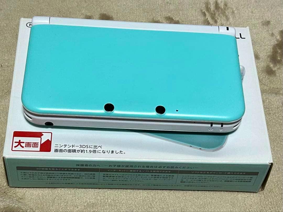 A mint and white Nintendo 3DS LL console shown closed on top of its box.