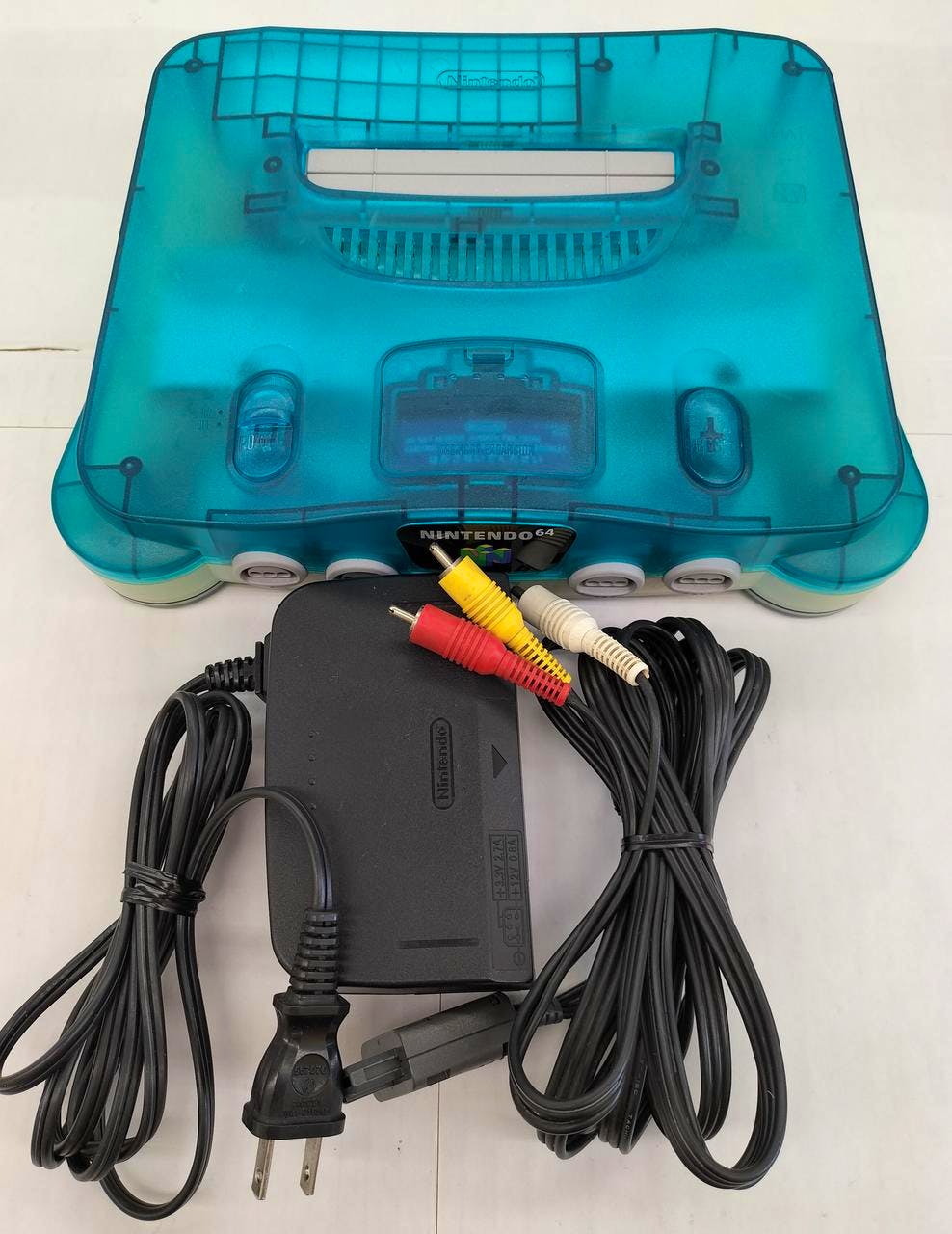 Turquoise translucent Nintendo 64 console pictured with a power adapter and composite AV cable on a white background.