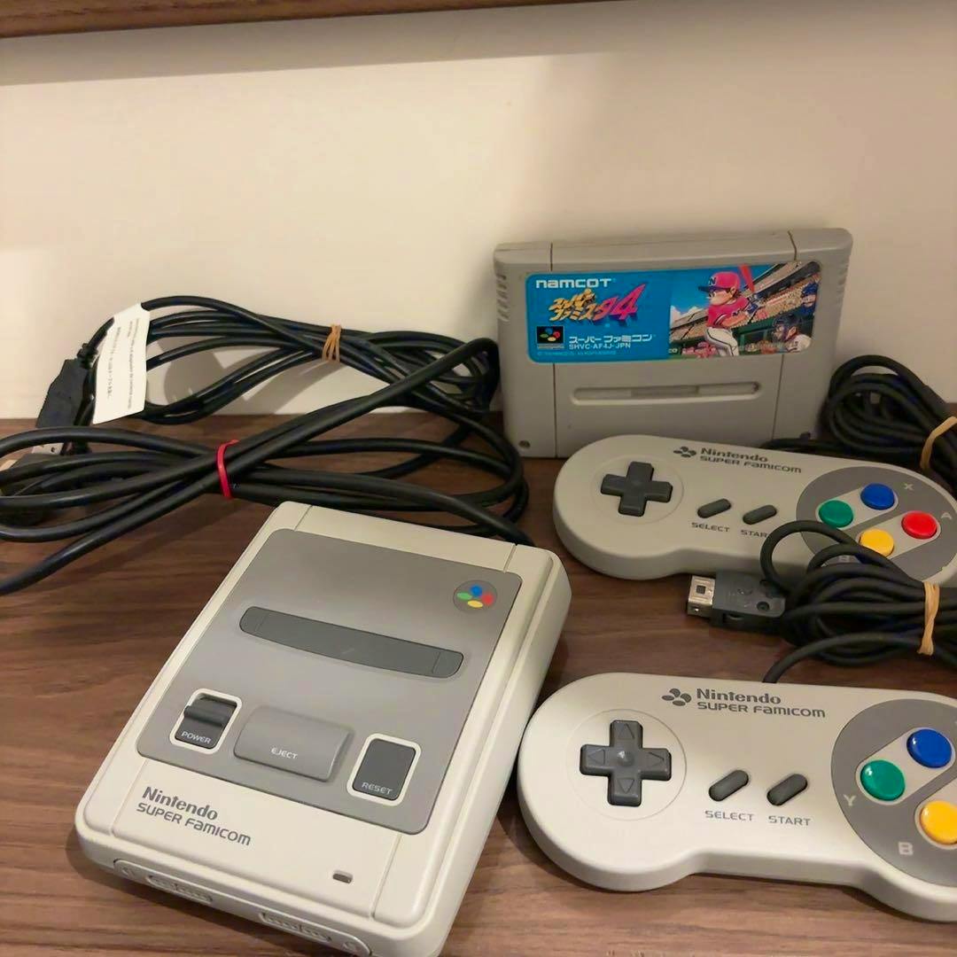 Nintendo Classic Mini Super Famicom console on a wooden surface with two controllers, cables, and a game cartridge visible.