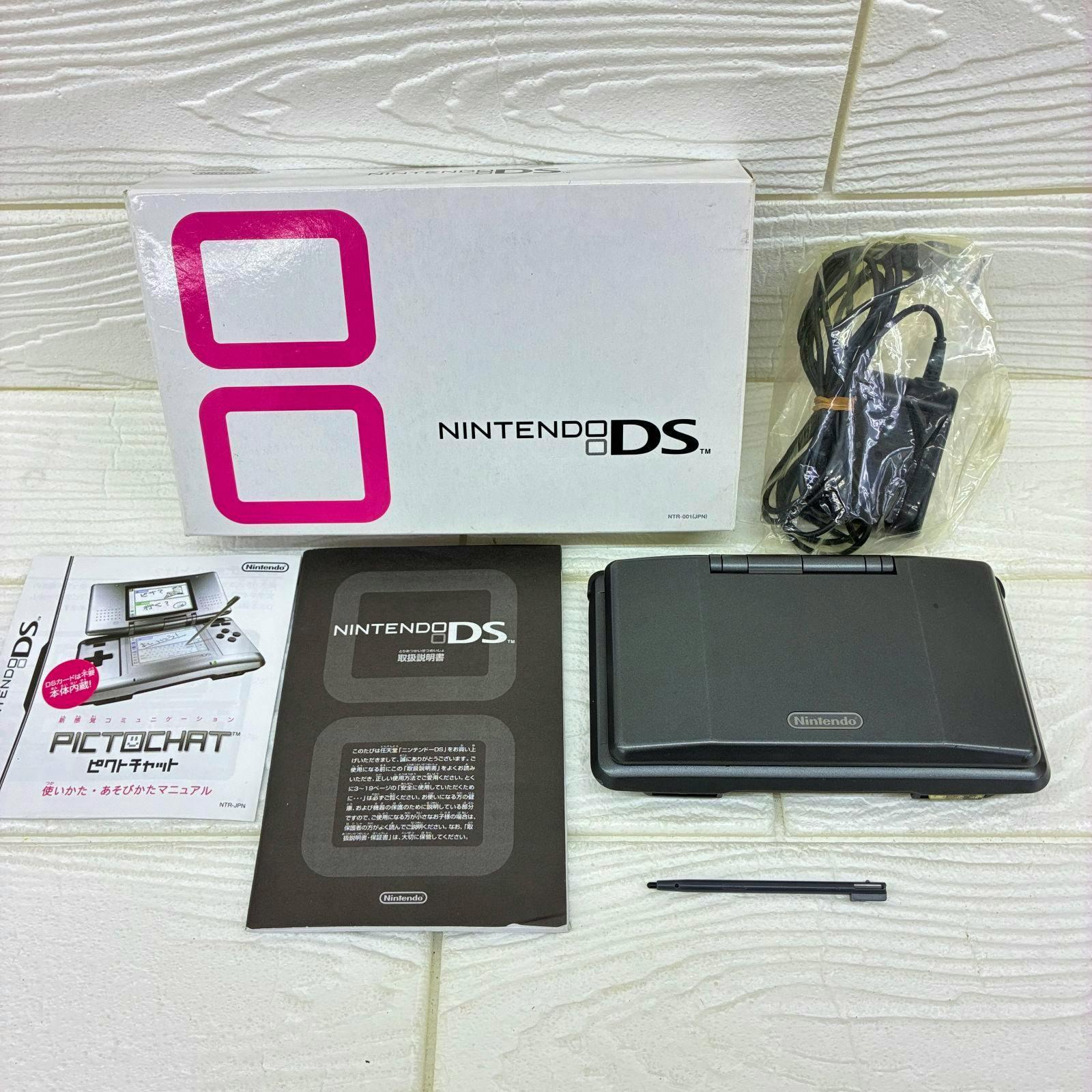 Closed original Nintendo DS (NTR-001) handheld shown with its box, manuals, charger and stylus on a white surface.