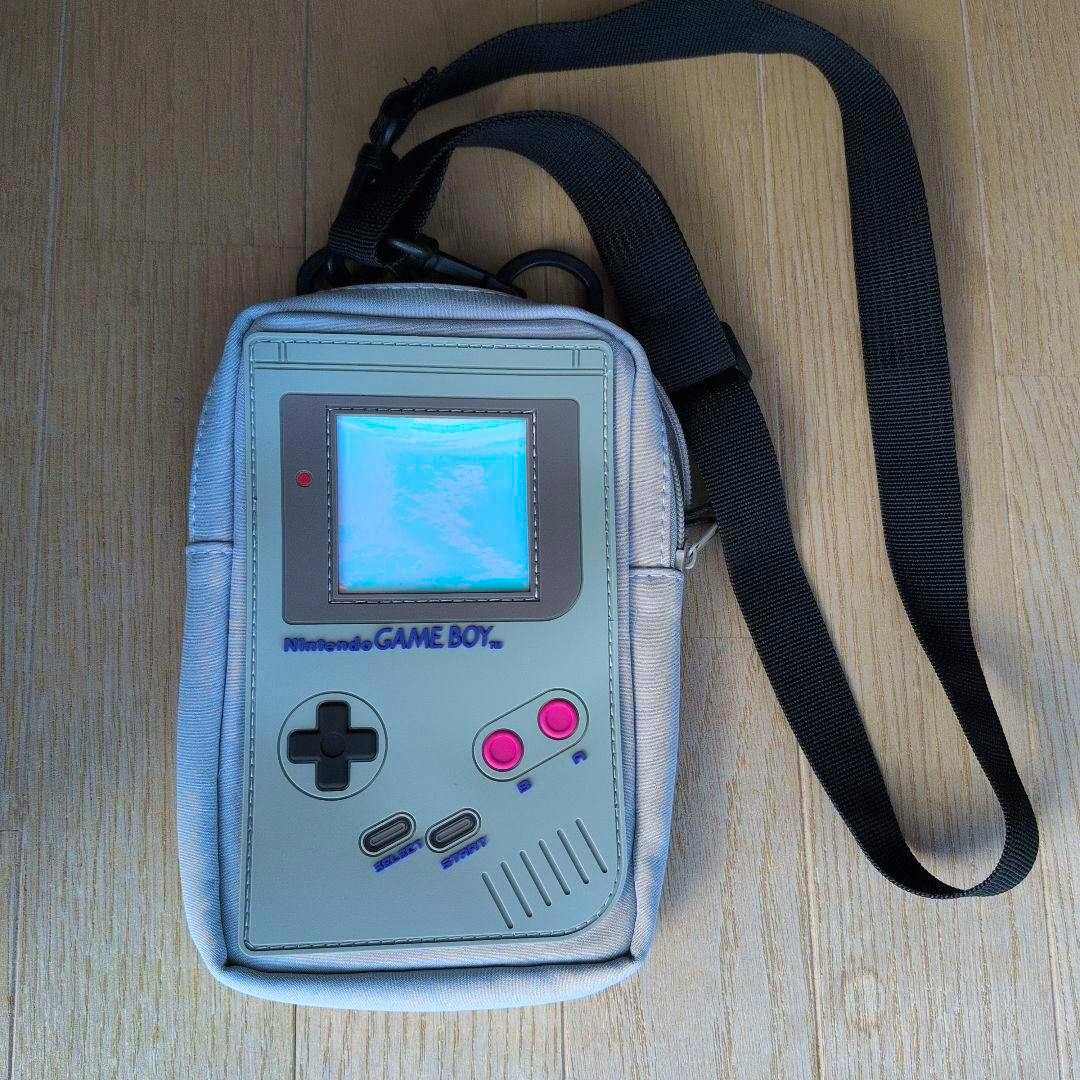 Front of the Nintendo GAME BOY shoulder pouch showing a Game Boy console graphic and an attached black shoulder strap on a wooden floor.