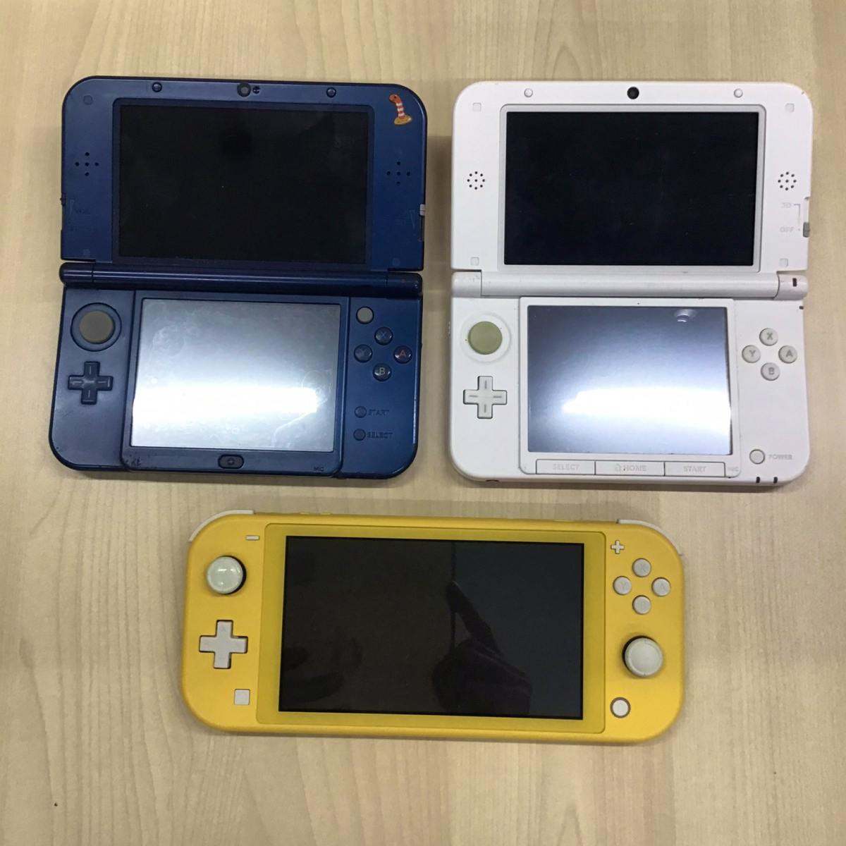 Three Nintendo handheld consoles arranged on a table: two 3DS-family systems at top and a yellow Nintendo Switch Lite at the bottom.