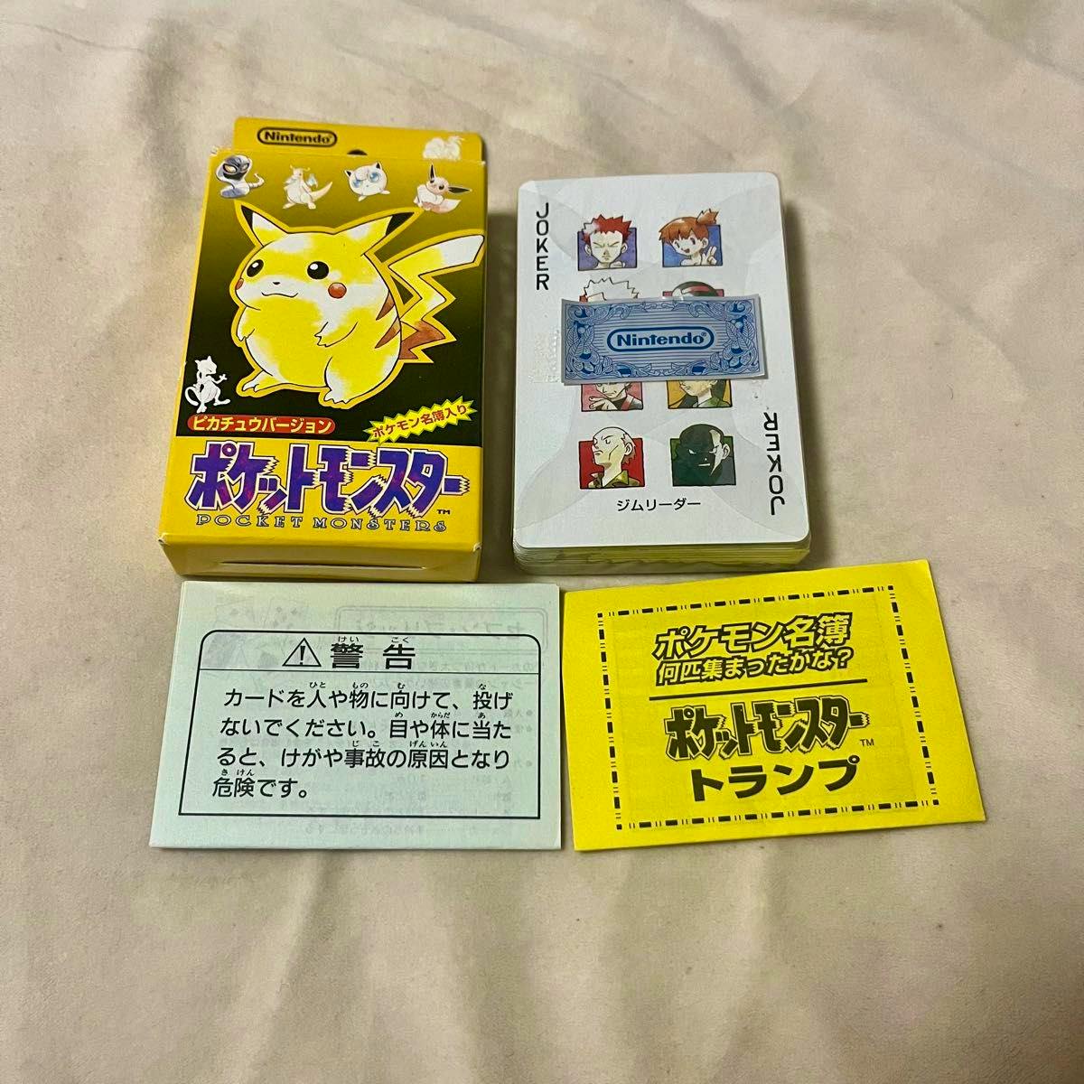Yellow Pikachu-version Pocket Monsters playing card box with a stack of cards and two paper inserts on a beige surface.