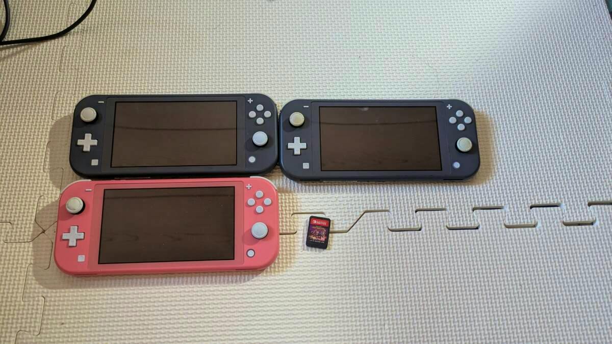 Three Nintendo Switch Lite consoles shown front-facing with one game cartridge on a mat.