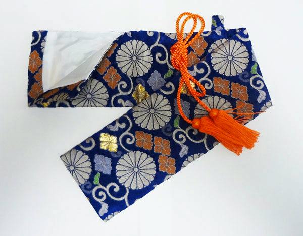 Polyester short-sword (6 sun) case with Nishijin-style silver-ran chrysanthemum pattern and attached orange tassel, shown open to reveal white lining.