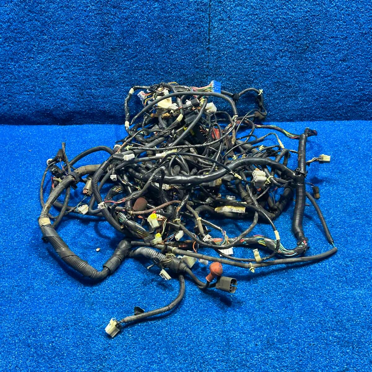 Wiring harness for a Nissan Figaro FK10 with multiple connectors and protective tubing laid on a blue carpeted background.