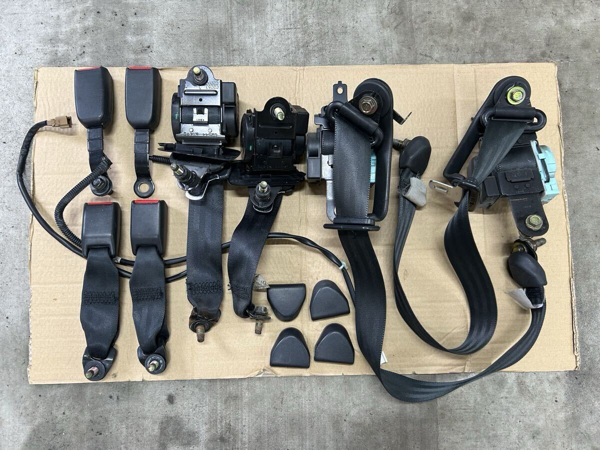 Laid-out Nissan car seat belt set on cardboard showing retractors, buckles, and belt assemblies.