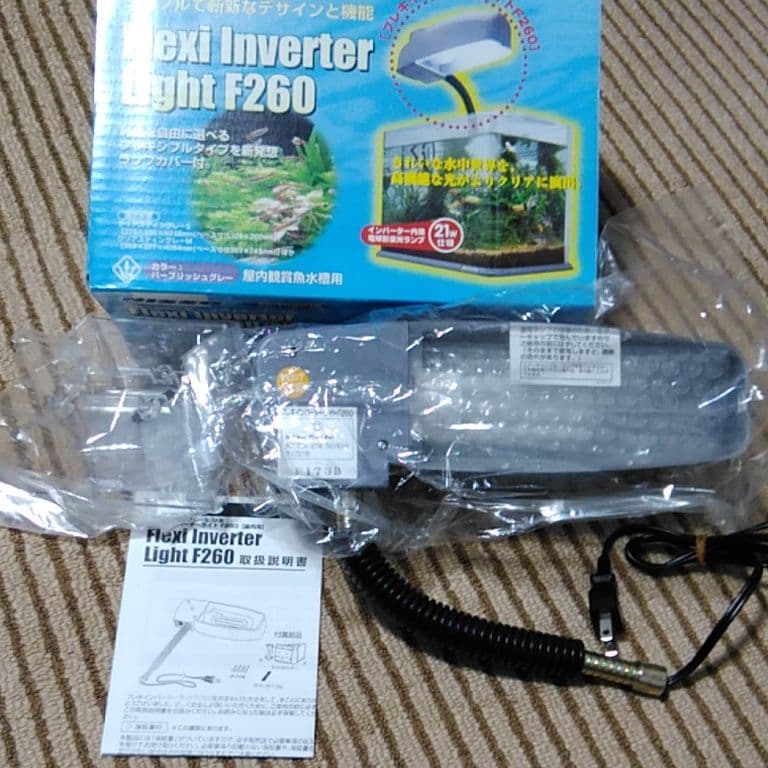 Packaged aquarium lamp unit with its coiled power cord, instruction manual, and product box on a carpet.
