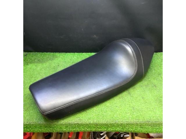 Black SR400/NitroHeads cafe motorbike seat displayed on a green surface against a dark background.