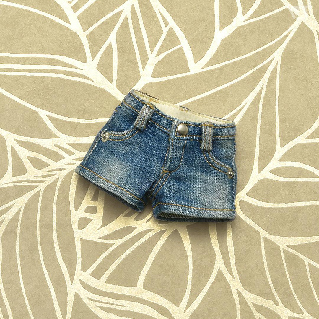 Blue mini denim shorts for a doll photographed on a patterned beige background.