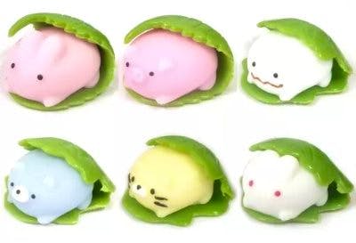 Six small plastic figures resembling sakura-mochi and kashiwa-mochi, each tucked under a green leaf, shown on a white background.