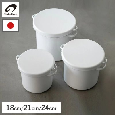 Three white round enamel storage pots with lids and side handles in small, medium, and large sizes on a gray surface.